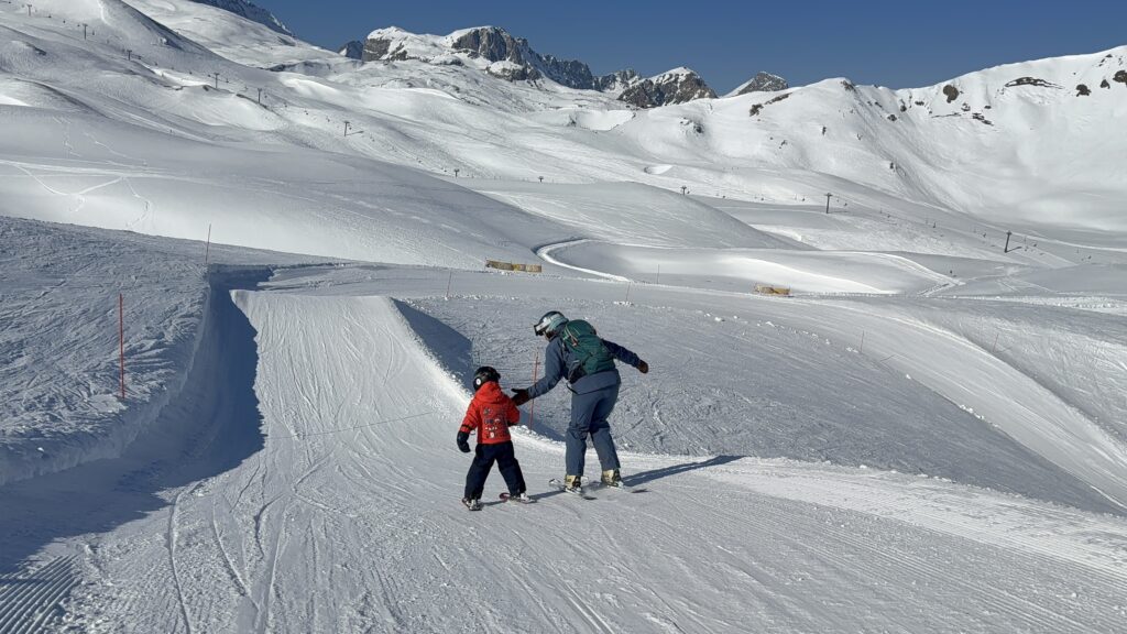 Ski instructor guiding a young child down a groomed slope in the mountains