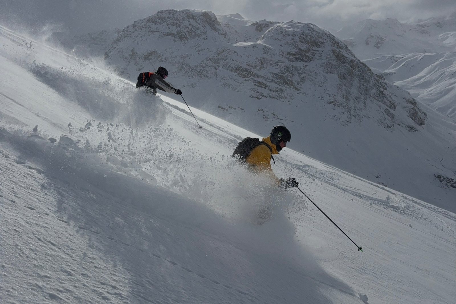 Deux skieurs en descente dans la neige fraîche, avec un nuage de poudreuse